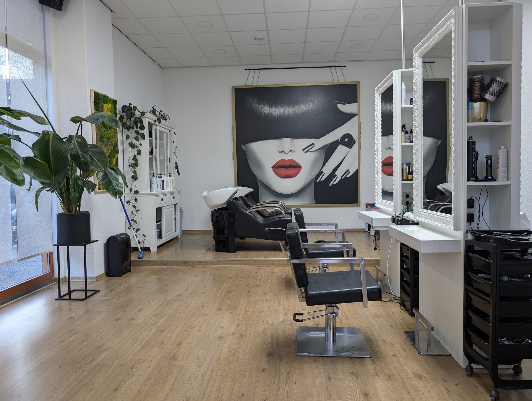 De salon met wasplek, werkplekken met witte spiegels en een groot zwart-wit portret met rode lippen aan de muur